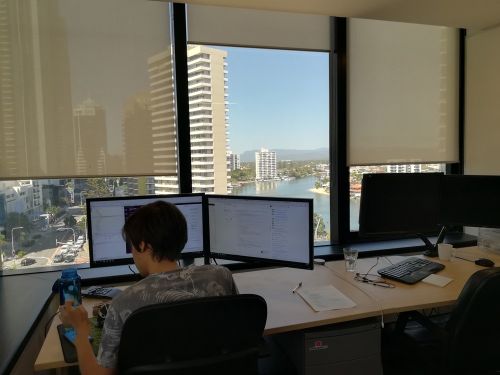 chica de espaldas sentada en un escritorio y enfrente de un ordenador y está en una oficina con vistas a edificios de Gold Coast